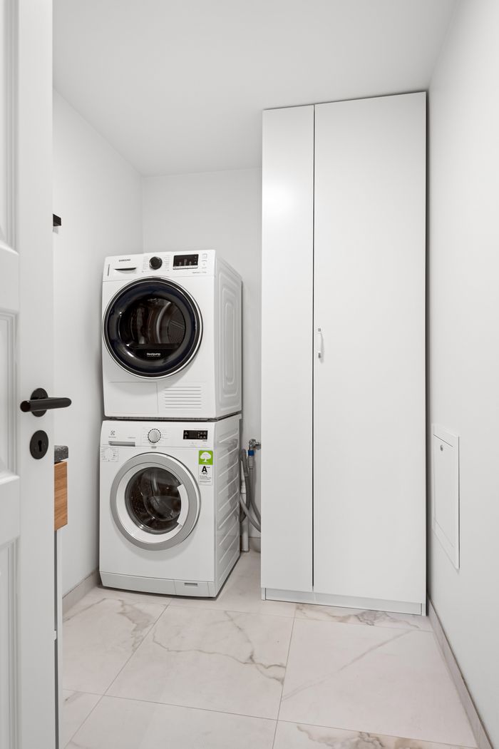our-story-02 Contemporary laundry room featuring stacked washer and dryer in a minimalist design.