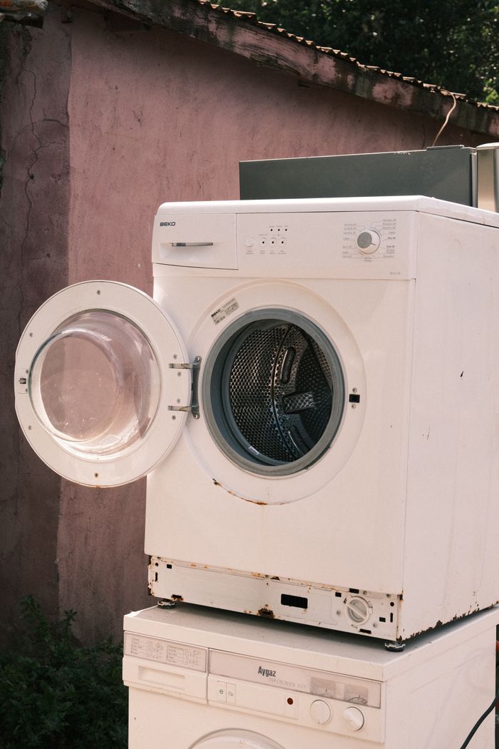 our-story-01 Outdoor view of two stacked laundry machines with an open door, showing rustic surroundings.